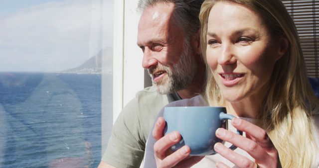 Couple enjoying peaceful moment by ocean, sipping coffee with beautiful view of coastline. Perfect for themes related to relationships, relaxation, travel, well-being, morning routines, and lifestyle.