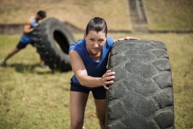 Fit woman flipping a tire during obstacle course in boot camp