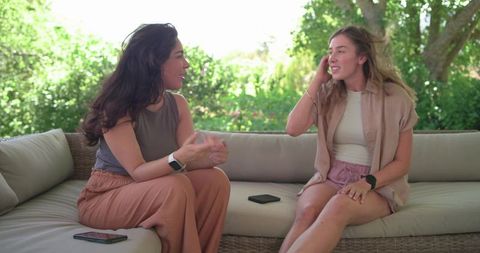 Diverse women chatting on outdoor wicker sofa enjoying sunny garden conversation