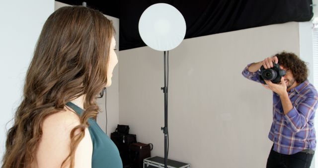 A young Caucasian woman poses for a photograph as a professional photographer captures her image, with copy space. They are in a studio setting, indicating a portrait photography session.