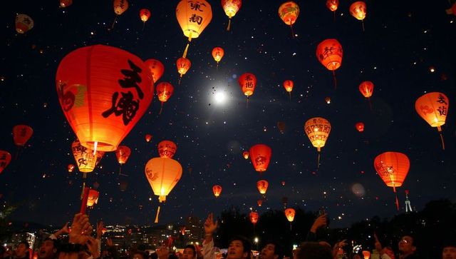 Moonlit sky lantern release over festival crowd, red paper lanterns floating into night