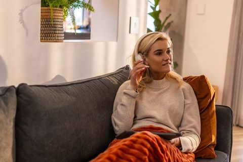 Blonde woman relaxing with wireless headphones and tablet on cozy modern living room sofa