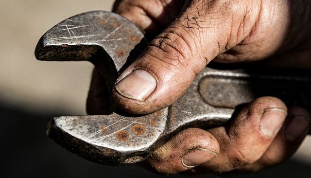 Gripping greasy hand holding rusted adjustable wrench close-up showing workshop hands