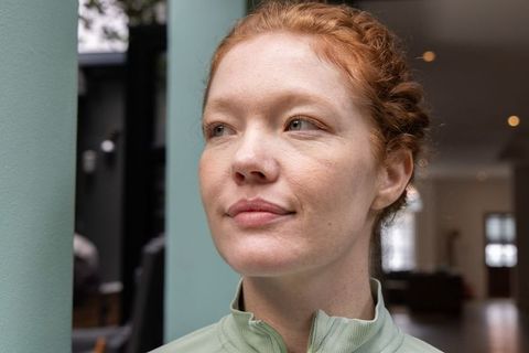 Serene redhead woman in light green zip-up top looking aside indoor portrait