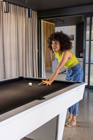 African american woman playing pool while leaning on table in modern recreation room