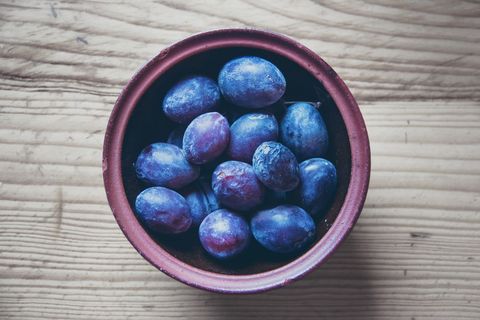 Rustic Ceramic Bowl Displaying Fresh Blue Plums on Light Wood Tabletop