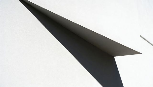 Minimalist Triangle Shadow Casting on White Plaster Facade with Folded Plane Geometry