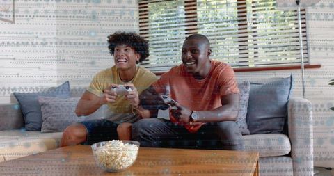 Playing competitive couch gaming in sunlit living room with controllers and popcorn