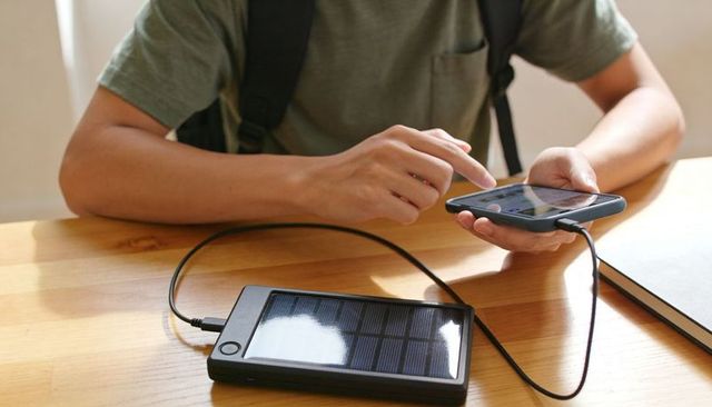Man charging smartphone with portable solar power bank on wooden desk