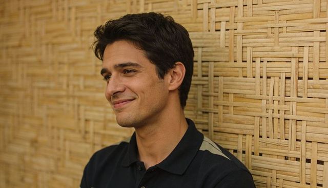 Relaxed young man leaning on woven bamboo wall at cafe smiling in casual polo