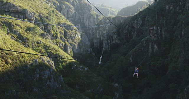 Person enjoying zip line ride over a lush green valley with mountains. Suitable for marketing travel destinations, outdoor adventure promotions, extreme sport highlights, and advertisements focusing on thrill-seeking activities.