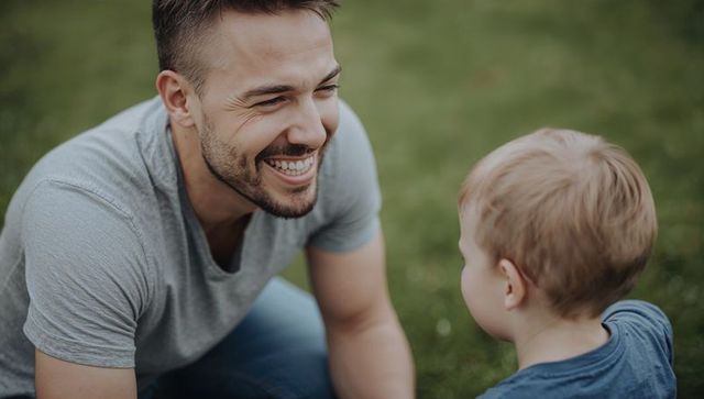 Father and young son sharing joyful moment on lawn, smiling dad leaning in outdoor bonding