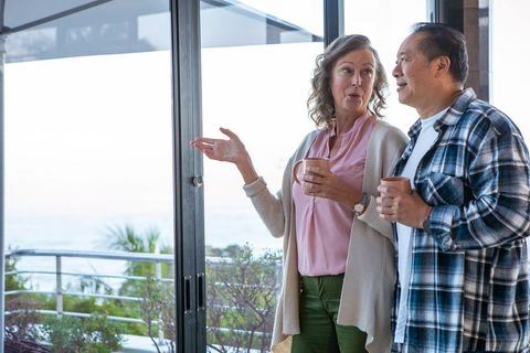 Senior Interracial Couple Chatting Near Glass Door Overlooking Ocean