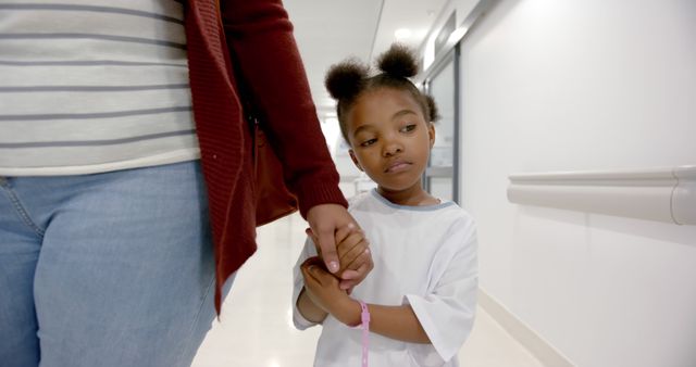 African american girl patient and her mother walking holding hands in corridor in hospital. Medicine, healthcare and hospital, unaltered.