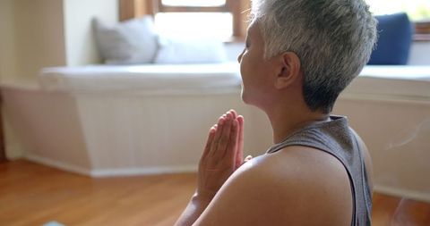 Senior woman meditating on yoga mat in peaceful home environment