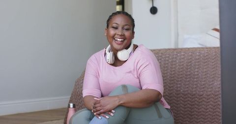 Smiling african-american woman relaxing at home in pink athleisure with headphones