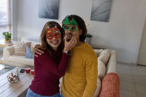 Couple celebrating holiday at home wearing festive novelty glasses and cozy knit sweaters