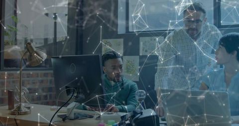 Diverse team collaborating around laptop in open-plan office with digital network overlay