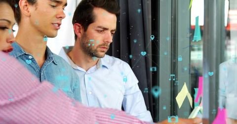 Team analyzing UX concepts on glass wall with sticky notes and digital icon overlays