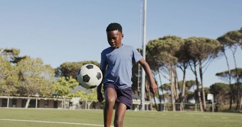 Young boy kicking soccer ball on sunny grass pitch practicing footwork and skills