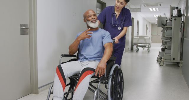 Asian female doctor walking with african american male patient sitting in wheelchair at hospital. Medicine, healthcare, lifestyle and hospital concept.