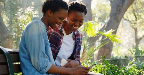 Twin Sisters Smiling and Using Mobile Phone in Sunlit Park