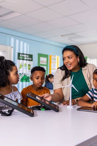Teacher guiding diverse elementary students in hands-on stem with wind turbine and tablets