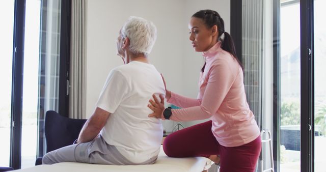 Image of happy biracial female physiotherapist exercising with caucasian senior man. seniors health and nursing home lifestyle concept digitally generated image.