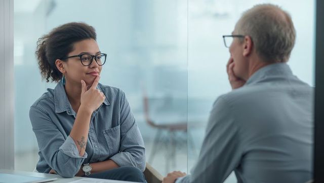 Contemplating woman consulting with colleague at glass-partitioned office meeting