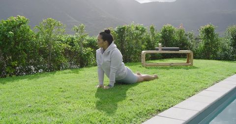 Woman practicing yoga outdoors near pool with mountain view