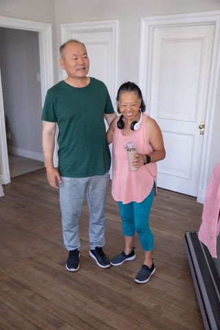 Asian senior couple smiling after indoor cardio workout with water bottle and headphones