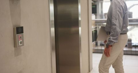 Businessman by elevator in modern office workspace holding laptop