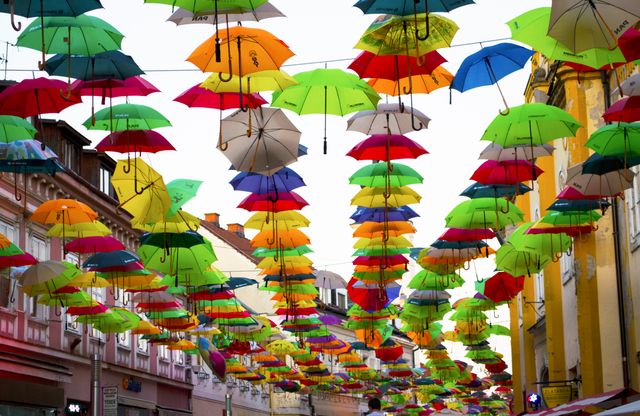 Colorful umbrellas suspended above a street in a European town, creating a vibrant and festive atmosphere. Use for themes related to travel, urban art installations, creative city spaces, and outdoor decorations.