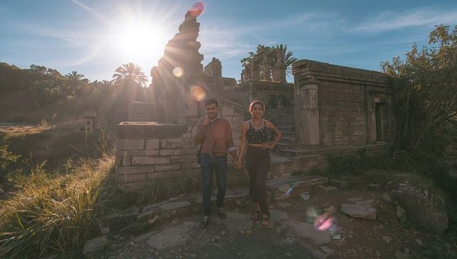 Couple holding hands at ancient stone ruins during golden hour with dramatic sun flare