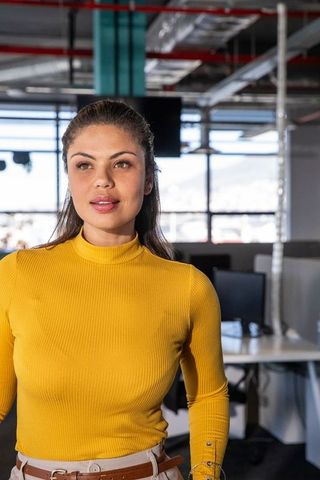 Confident woman in mustard top standing and glancing right in modern office workspace