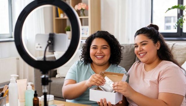Latina beauty creators unboxing skincare kit on sofa with ring light and smiling faces