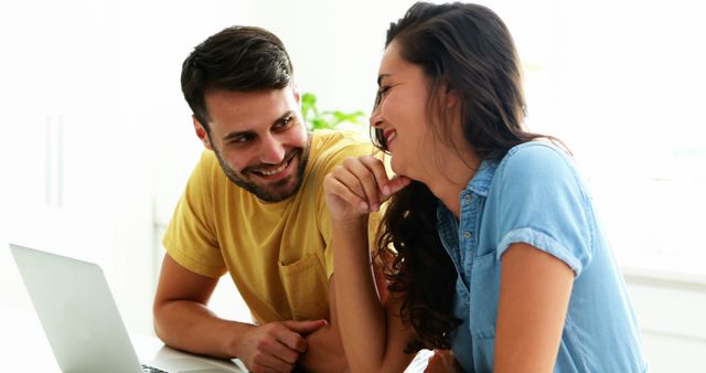 Couple laughing and enjoying time together at home while using laptop, showcasing modern household lifestyle, happiness, and technology bonding. Perfect for advertising family software products, relationship articles, or home technology trends.