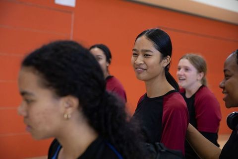 Diverse teen athletes smiling and chatting in school corridor wearing maroon black jerseys