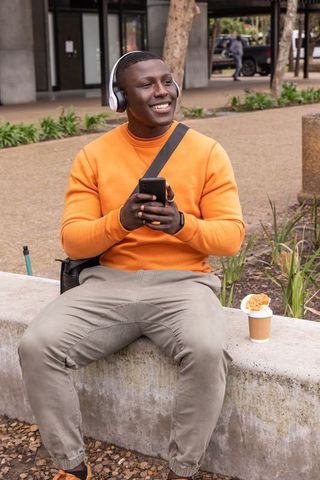 Smiling african american man listening to music using smartphone on urban concrete bench