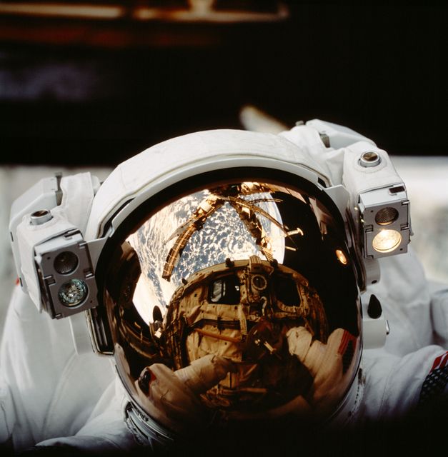 The image depicts an astronaut in a space helmet featuring a reflection of the space shuttle Atlantis, the Mir space station, and Earth’s horizon. This captures a significant moment in space exploration history. The photograph can be utilized for educational materials, aerospace industry promotions, historical documentation, space travel posters, and inspiring space-related visuals.