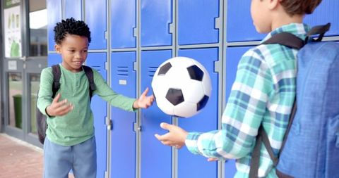 Happy Students Playing with Soccer Ball by School Lockers