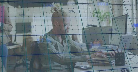 Typing young professional at laptop with digital analytics overlay in modern open office