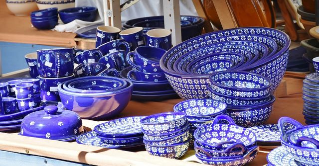 Variety of blue ceramic tableware featuring intricate designs on display at an outdoor market stall. Ideal for images focused on kitchen decor, handmade crafts, artisanal products, or market scenes. Perfect for advertising handmade and unique kitchenware and pottery.