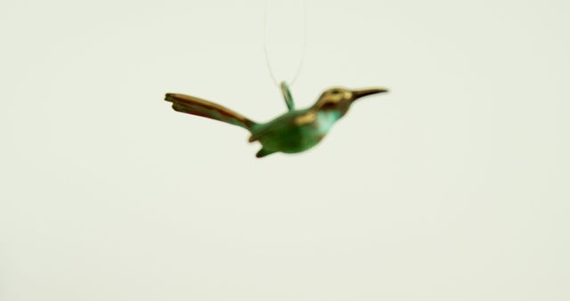 A green hummingbird ornament is suspended in mid-air against a plain background, with copy space. Its delicate features and poised wings capture the essence of the bird's graceful flight.