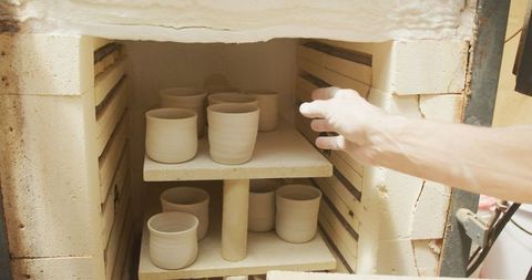 Senior Man Carefully Firing Pots in Pottery Kiln Workshop