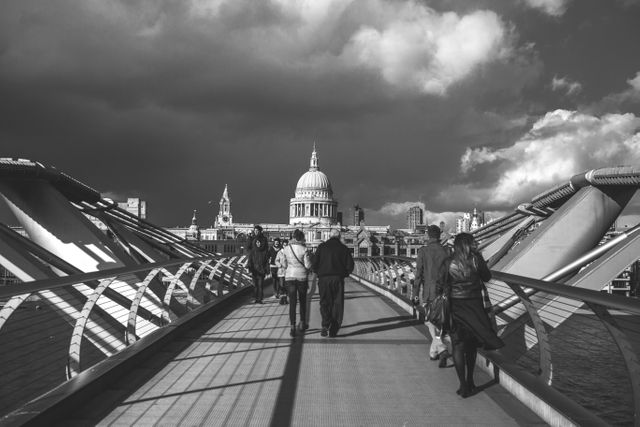 Shows people walking on Millennium Bridge in London with St. Paul's Cathedral visible in the background. Black and white photo emphasizing architectural details and contrast. Suitable for travel blogs, articles on London landmarks, urban photography enthusiasts, tourism guides, or historical architecture features.