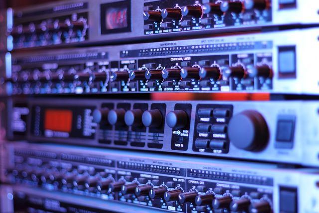 Close-up of professional rack mounted audio equipment featuring control knobs, buttons, and digital displays, commonly used in music production and sound engineering. Ideal for illustrating high-tech audio setups, recording studios, live sound engineering equipment, and professional audio control.