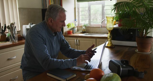 Senior Man Browsing Smartphone and Laptop at Kitchen Table - Download Free Stock Images Pikwizard.com