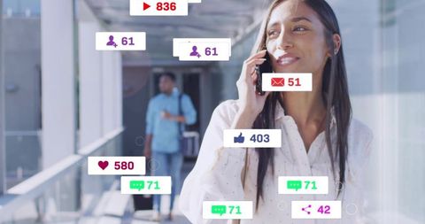 Smiling woman talking on phone with floating social media notifications in glass corridor