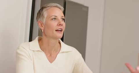 Mature woman speaking in calm conversation at home, short gray hair, cream sweater closeup